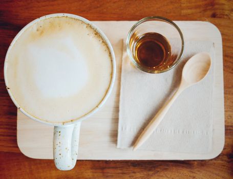 Cappuccino or latte coffee on wooden tray with syrup, retro filter effect