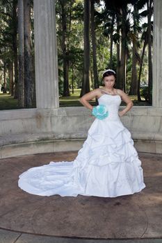 A lovely young bride outdoors wearing her wedding gown and holding her boquet, with an angry or frustrated facial expression.