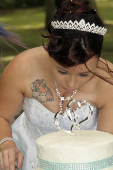 A lovely young bride cuts her wedding cake outdoors.