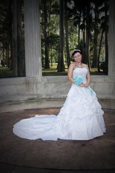 A lovely young bride outdoors wearing her wedding gown and holding her boquet.