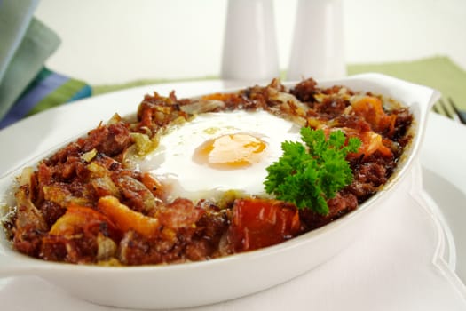 Baked corned beef hash with egg, tomato and onion with parsley.