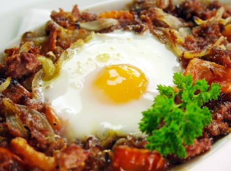 Baked corned beef hash with egg, tomato and onion with parsley.