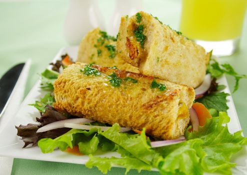 Vegetarian baked corn rolls dripping with parsley butter on a bed of mixed lettuce.