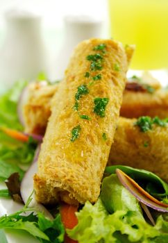 Vegetarian baked corn rolls dripping with parsley butter on a bed of mixed lettuce.