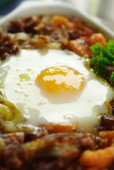 Baked corned beef hash with egg, tomato and onion with parsley.