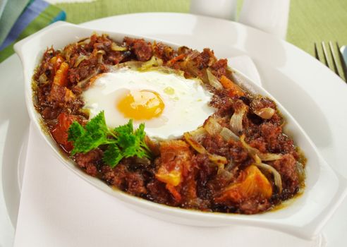 Baked corned beef hash with egg, tomato and onion with parsley.