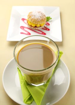 Glass of latte with custard tart in the background.