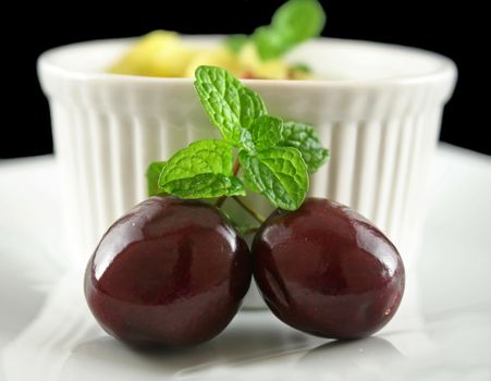 Two cherries with mint garnish with a dessert bowl.