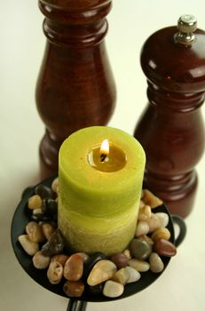 Salt and pepper grinders with a candle set in stones with subdued lighting.
