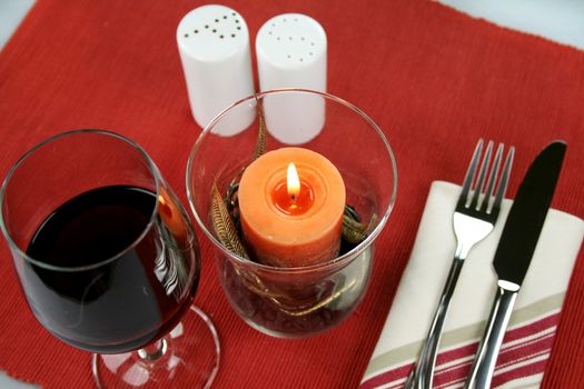 Dinner decor with an ornate candle, cutlery, salt and pepper shakers and a glass of red wine.