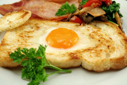 Egg embedded in toast with bacon, mushrooms, spinach and tomatoes.