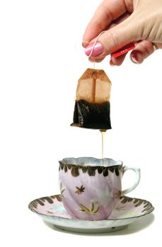 Dripping tea bag held above an antique teacup and saucer.
