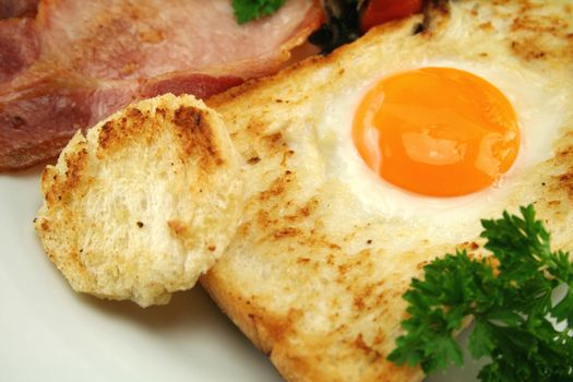 Delicious breakfast of fried egg embedded in toast with bacon and parsley.
