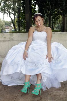 A lovely young bride, seated outdoors, proudly displays her new shoes.
