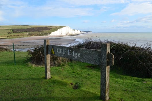 Wooden sign warning of a cliff edge.Image of the Seven Sisters in the background.