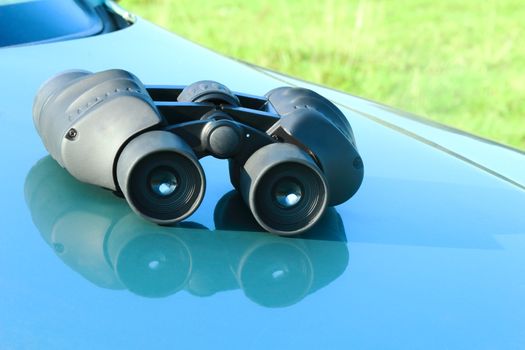 On the hood of a blue car is the binoculars.
