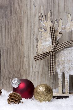 christmas decoration with wood background, snow, elk, christmas baubles gold and red and pine cones 