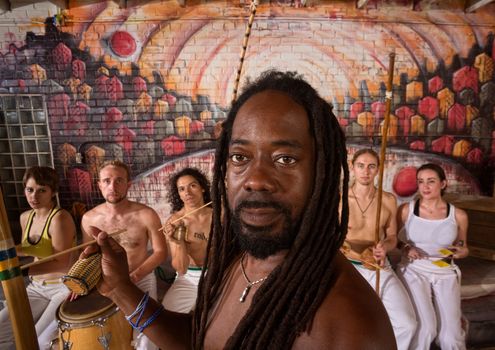 Handsome African capoeira master with students playing music