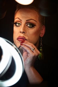 Serious Caucasian drag queen using lipstick