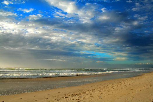 Sandy beach bathed in the early morning light with cloudscape.