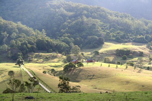 Sun bursting over a farm house in a rolling valley.