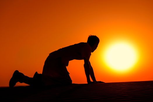 Tired and weaken man on all fours with gold sunset sun disk on background