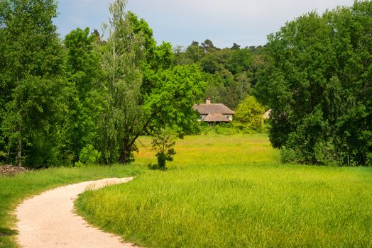 Green country area with path, agriculture field and traditional village house, Eastern Europe