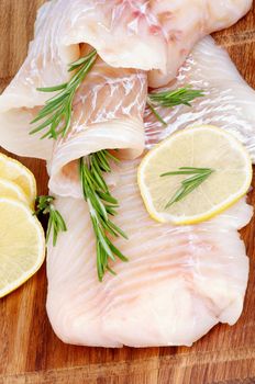 Raw Cod Fish Fillet with Lemon Slices and Rosemary closeup on Wooden background. Vertical View