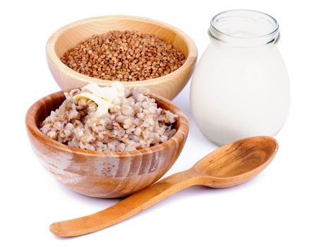 Arrangement of Traditional Russian Buckwheat Kasha with Buckwheat in Wooden Bowl, Milk Jar and Wooden Spoon isolated on white background
