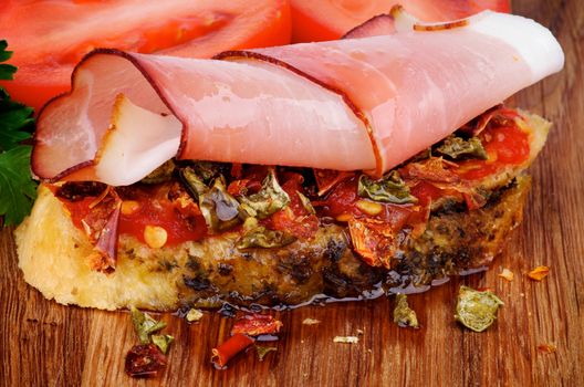 Delicious Spanish Tapas with Cured Ham Prosciutto, Slices of Paprika, Pepper, Toast and Olive Oil closeup on Wooden background