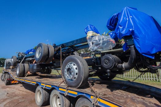 New built truck chassis frame wheels and engines on transport trailer.