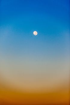 Full moon with colors in the early morning blue sky