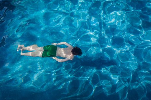 Young boy swimming in pool outdoors underwater.