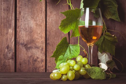 Grapes with leaves and glass of wine on the wood background