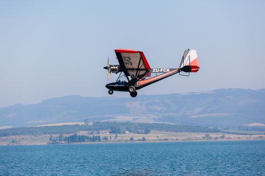Pilot in light microlight aircraft flying low over dam waters.