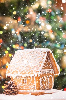 gingerbread house over defocused lights of Chrismtas decorated fir tree and snow