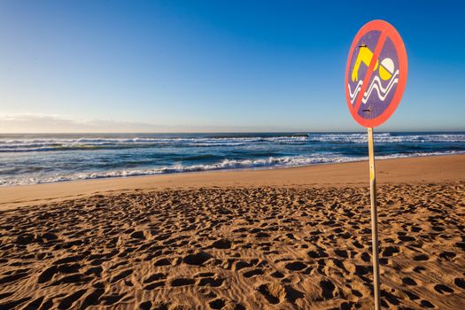 Large ocean waves pounding beach shoreline with lifeguard sign warnings no-swim to public