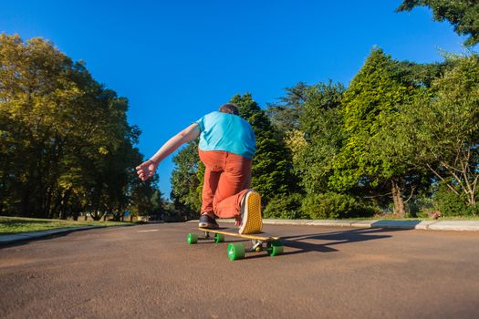 Teenager boy having fun skateboarding down small home tarred road in afternoon sunlight.