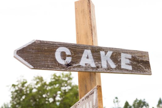 A handmade sign reads cake at an outdoor summer wedding pointing guests to the dessert table.