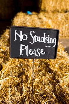 A chalkboard sign at a wedding reception reads no smoking please and is placed on a hay bail.