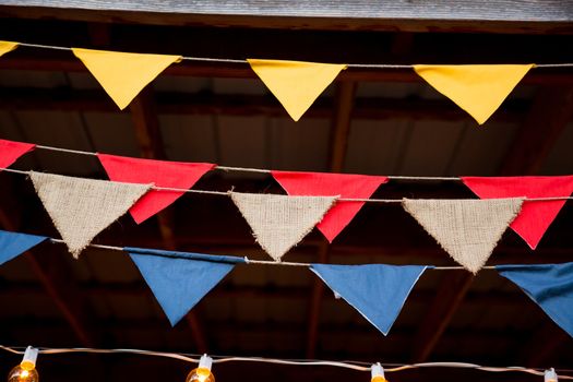 Wedding decor consists of multi colored flags in red, burlap, yellow, and blue for this outdoor country wedding ceremony and reception.