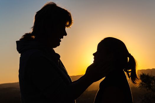 Mother daughter affection caring moments together silhouetted outlines at sunset.