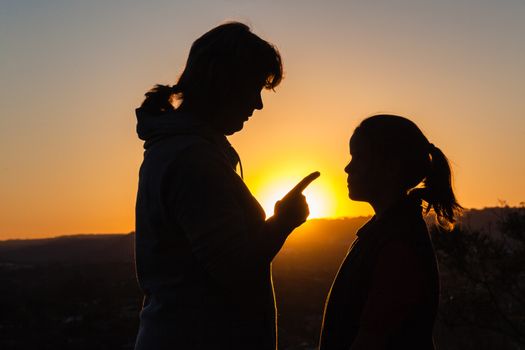 Mother daughter discipline warning instruction silhouetted body outlines at sunset.