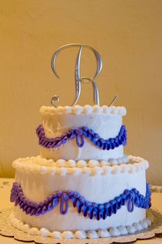 A cake topper with the letter R on it on this white and purple cake indoors.