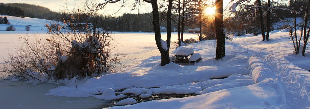 Winter landscape with snow and picnic table at sunset.