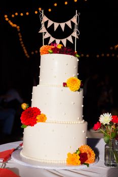 A handmade cake topper has flags that say just married on it above the wedding cake at this reception party.