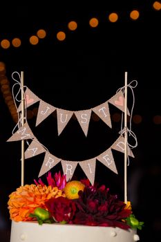 A handmade cake topper has flags that say just married on it above the wedding cake at this reception party.