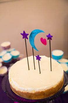 This handmade cake topper has a moon, heart, and stars on it above a wedding cheesecake.