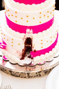 A wedding cake has a missing slice after the bride and groom cut the cake at their reception.
