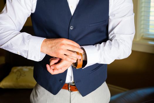 A groom fastens his watch on his wrist while getting ready for a wedding day celebration.